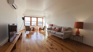 A spacious living room with a wooden floor, a sofa, a coffee table, and a TV on a stand.