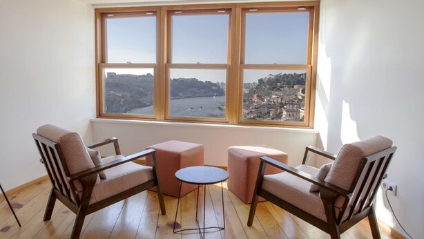 A room with a large window, two armchairs, a small round table, and a pink ottoman.