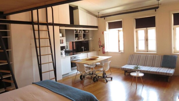 Un espace de vie compact comprenant une chambre en mezzanine, un coin cuisine et un espace salon avec vue sur l’extérieur.