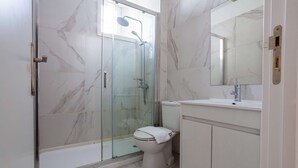 Une salle de bain avec une douche à parois de verre, des toilettes blanches et un lavabo avec un miroir au-dessus.