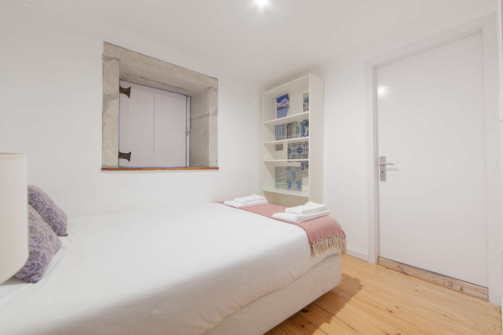 A bedroom with a bed, a wardrobe, a shelf with decorative items, and a door.