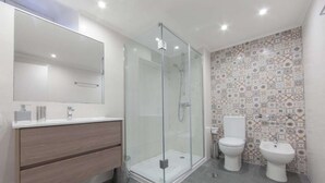 Un bagno moderno con doccia vetrata, mobile lavabo in legno, due servizi igienici e schienale piastrellato.