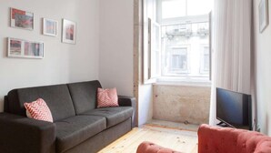 Un soggiorno con un divano grigio, una poltrona rossa, una televisione a schermo piatto e una finestra con vista sugli edifici.