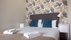 A neatly made bed with white linens and a beige blanket, flanked by two white nightstands with lamps. - One-bedroom apartment with a sofa bed (Porto)