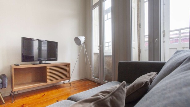 A living room with a TV on a wooden stand, a floor lamp, and a grey sofa. - One-bedroom apartment with a sofa bed (Porto)
