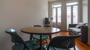 A small, well-lit room with a round table and four chairs, a television on a small stand, and a sofa. - One-bedroom apartment with a sofa bed (Porto)