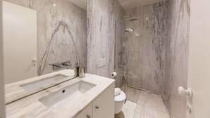 A modern bathroom with a marble sink, a glass shower enclosure, and a toilet. - Suite with a double bed and air conditioning (Porto)