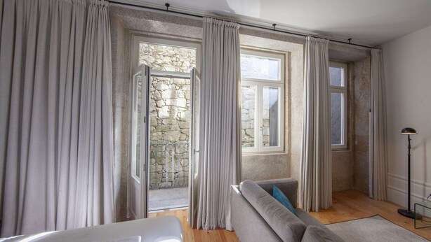 A room with a stone wall, a sofa, and a window with curtains. - Suite with a double bed and air conditioning (Porto)