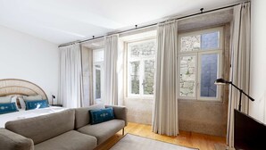 A modern bedroom with a sofa, a bed, and a large window with curtains. - Suite with a double bed and air conditioning (Porto)