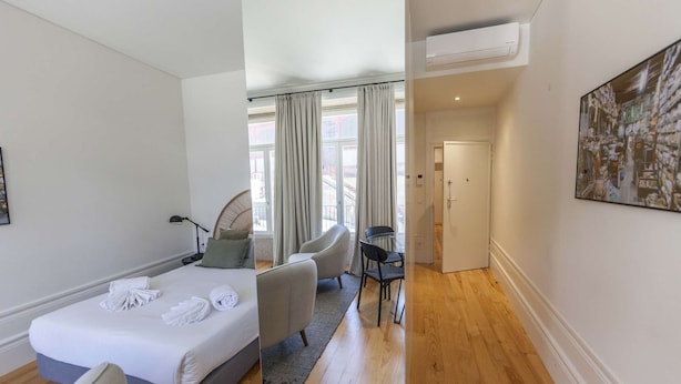 A hotel room with a bed, a seating area with chairs, a small table, and a door leading to another room. - Suite with a view to the city, double bed and air conditioning (Porto)