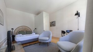 A modern bedroom with a bed, two armchairs, a desk with a computer, and a floor lamp. - Suite with a view to the city, double bed and air conditioning (Porto)