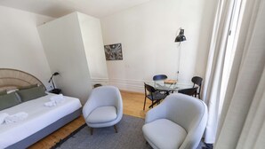 A small, modern room with a bed, two armchairs, a small table, and a desk. - Suite with a view to the city, double bed and air conditioning (Porto)