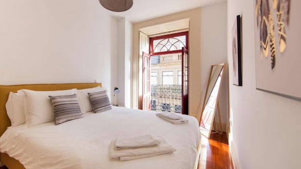 Una cama bien hecha con sábanas blancas y toallas dobladas, cabecera de madera y una lámpara colgante.