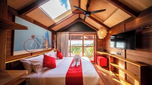 A wooden cabin-style room with a bed, a bicycle, a TV, and a balcony with a view. - SOKKOOL CANGGU - COWORKING & COLIVING (Tibubeneng)