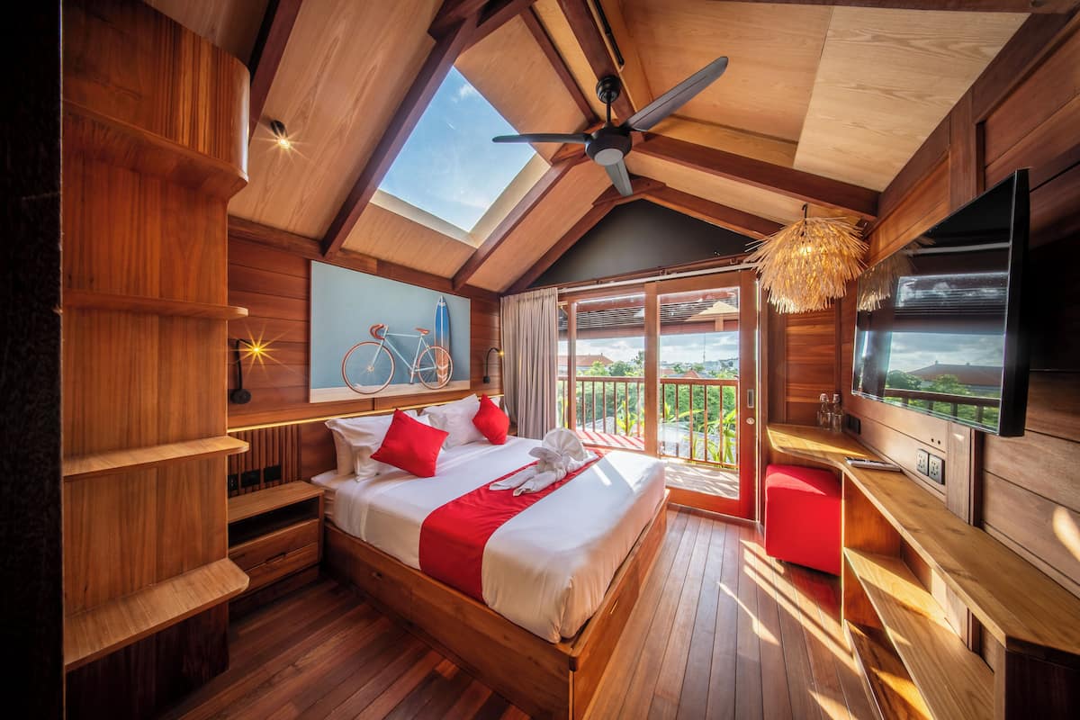 A wooden bedroom with a large bed, a ceiling fan, a TV, and a balcony with a view.