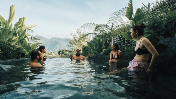 A group of people in a natural pool surrounded by tropical vegetation and mountains in the background. - SOKKOOL CANGGU - COWORKING & COLIVING (Tibubeneng)