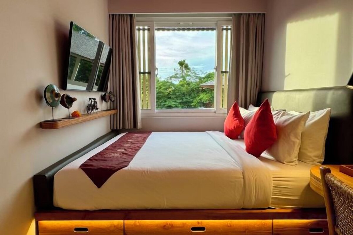 Habitación de hotel con cama, televisión, ventana con cortinas y vista a zonas verdes.