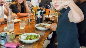 A group of people dining at a restaurant with a wooden table, various dishes, drinks, and a green wall with wavy patterns in the background. - SOKKOOL CANGGU - COWORKING & COLIVING (Tibubeneng)