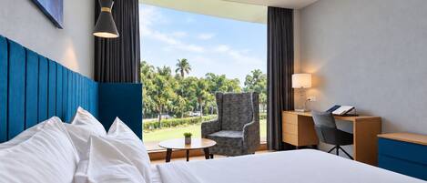 Habitación de hotel con una cama grande, un escritorio, una silla y vistas a palmeras.