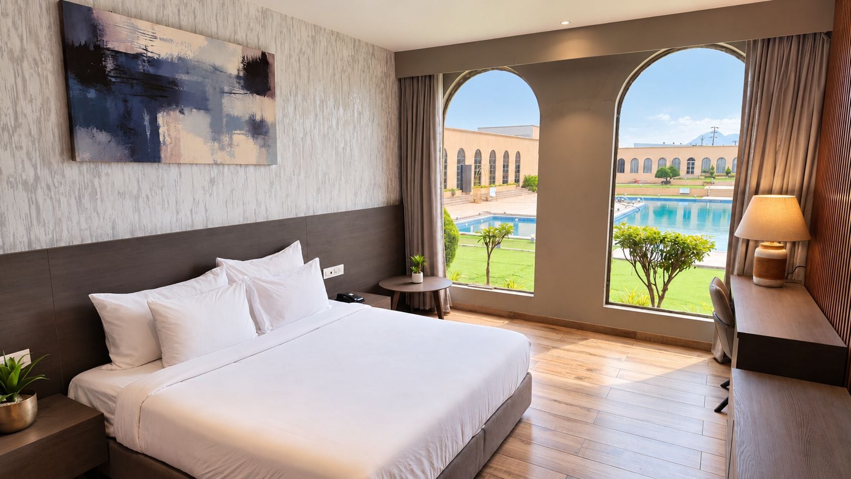 Habitación de hotel con una cama grande, un cuadro en la pared, y vistas a una piscina y un edificio a través de ventanas de arco.