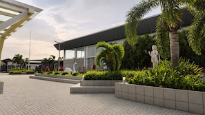 A modern building with a glass facade, surrounded by landscaped gardens and a paved walkway. - THE DEMOCRACY HOTEL & RESORT (Nashik)