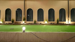 A building with a green lawn in front, large arched windows, and lights along the windows. - THE DEMOCRACY HOTEL & RESORT (Nashik)