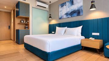 A modern hotel room with a large bed, a bedside table with a phone, a wardrobe, and a wall-mounted air conditioner.