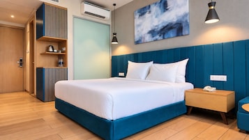 A modern hotel room with a large bed, a bedside table with a phone, a wardrobe, and a wall-mounted air conditioner.