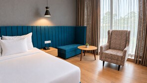 A hotel room with a bed, a blue sofa, a round table, and a patterned armchair. - THE DEMOCRACY HOTEL & RESORT (Nashik)