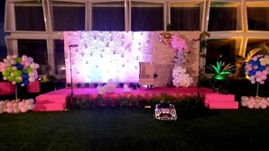 A stage with a floral backdrop, pink steps, and a white car in front. - THE DEMOCRACY HOTEL & RESORT (Nashik)