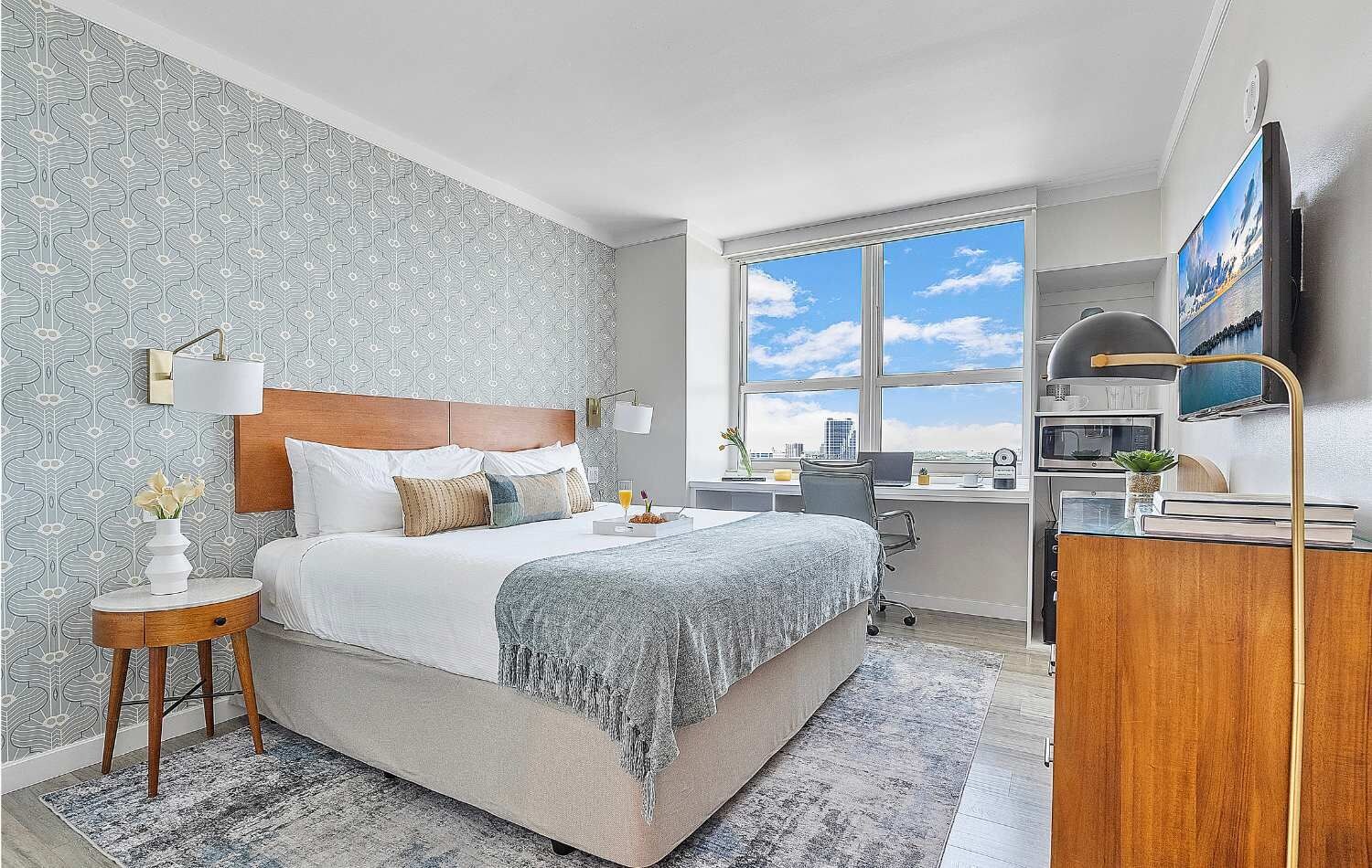 Ein Hotelzimmer mit Bett, Nachttisch, Lampe und Schreibtisch mit Stuhl.