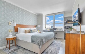 A hotel room with a bed, bedside table, lamp, and a desk with a chair.