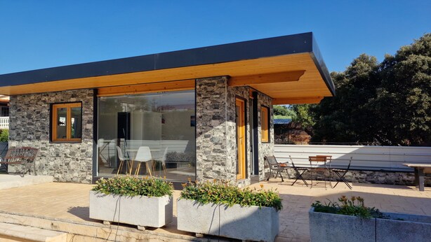 Un bâtiment moderne doté d’une façade en pierre, de grandes fenêtres en verre et de poutres en bois.