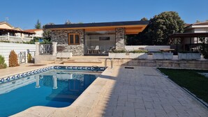 Une piscine avec un bord carrelé, un mur en pierre et une terrasse en bois.