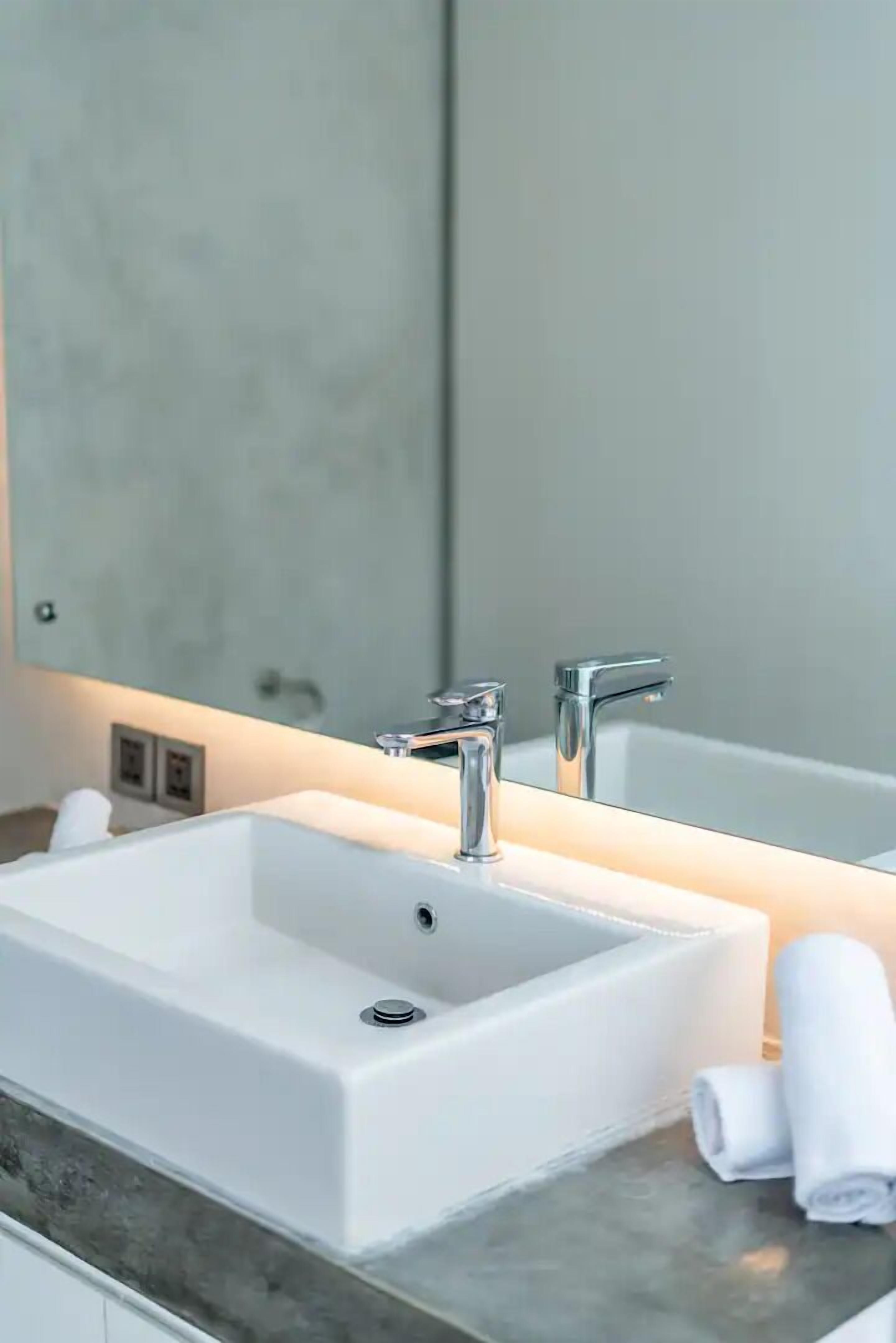 A modern bathroom with a white sink, two faucets, and a large mirror.