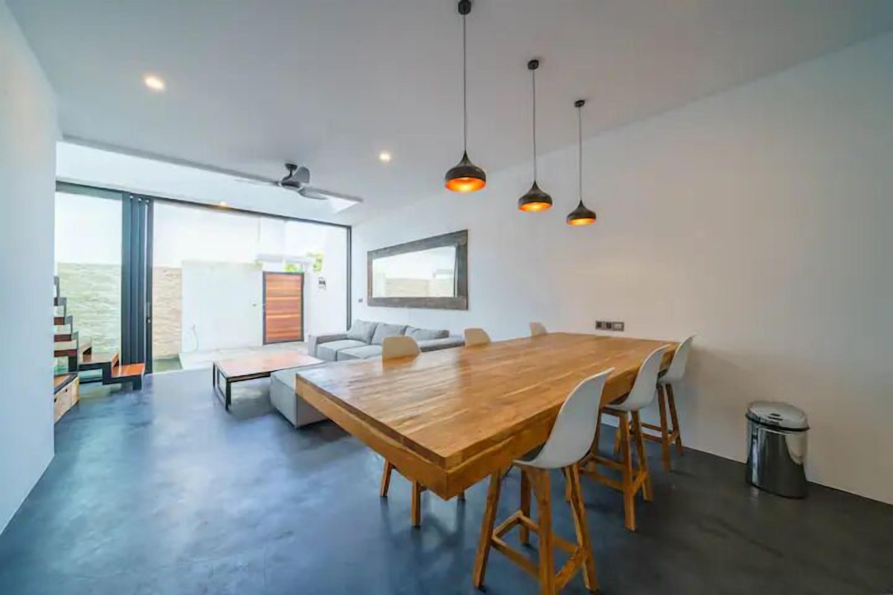A modern dining area with a wooden table and chairs, a sofa, and pendant lights.