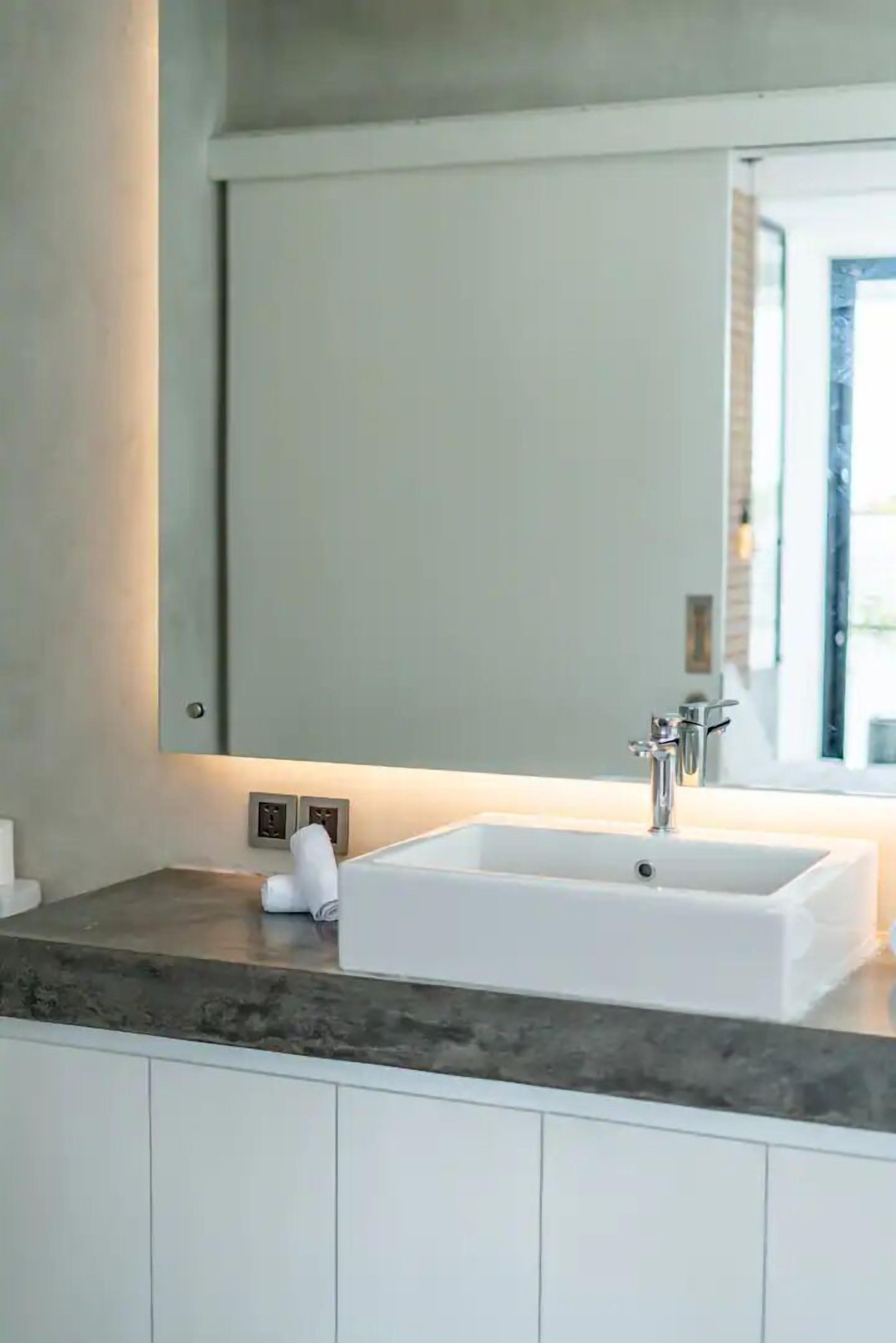Un baño moderno con un espejo grande, un lavamanos blanco y una encimera de mármol.