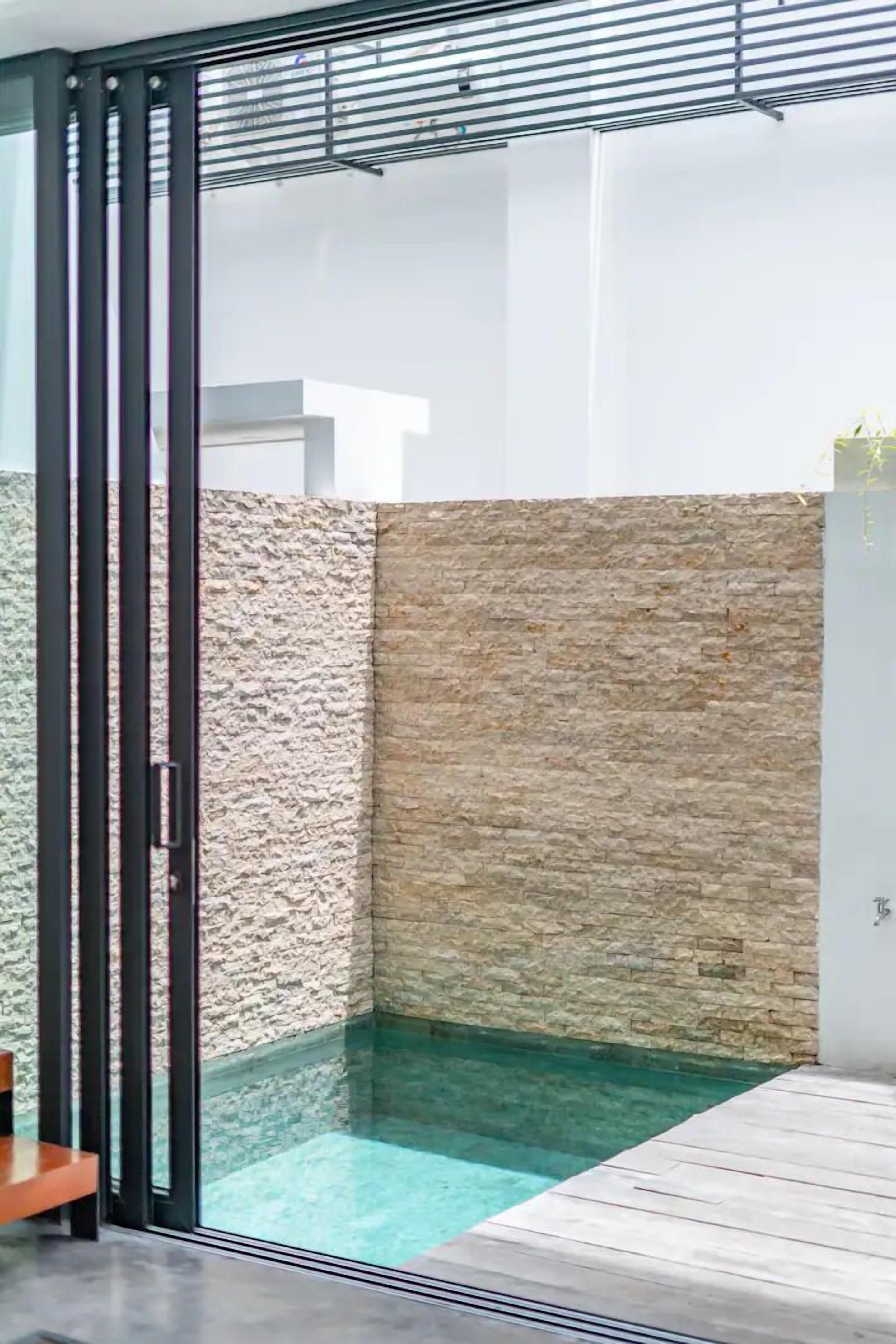A modern outdoor pool area with a glass enclosure, stone walls, and a wooden deck.