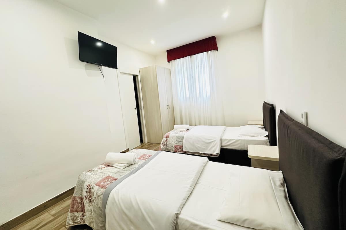 Une chambre d’hôtel avec deux lits, un téléviseur fixé au mur et une fenêtre avec des rideaux.