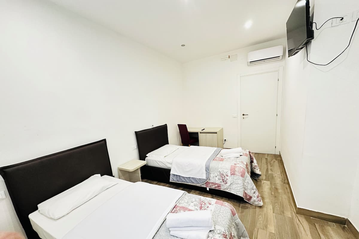 Une chambre d’hôtel avec deux lits simples, un bureau, une chaise et un téléviseur fixé au mur.