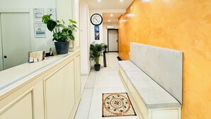 A hotel reception area with a counter, potted plants, a clock, and a bench. - Dream Hub (Mestre)