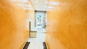 A hallway with a glossy, warm-toned wall and a tiled floor, leading to a reception area with a desk and chairs. - Dream Hub (Mestre)