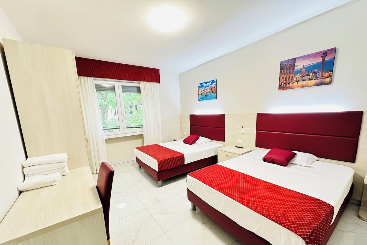 Une chambre d’hôtel avec deux lits, un bureau et une fenêtre avec des rideaux.