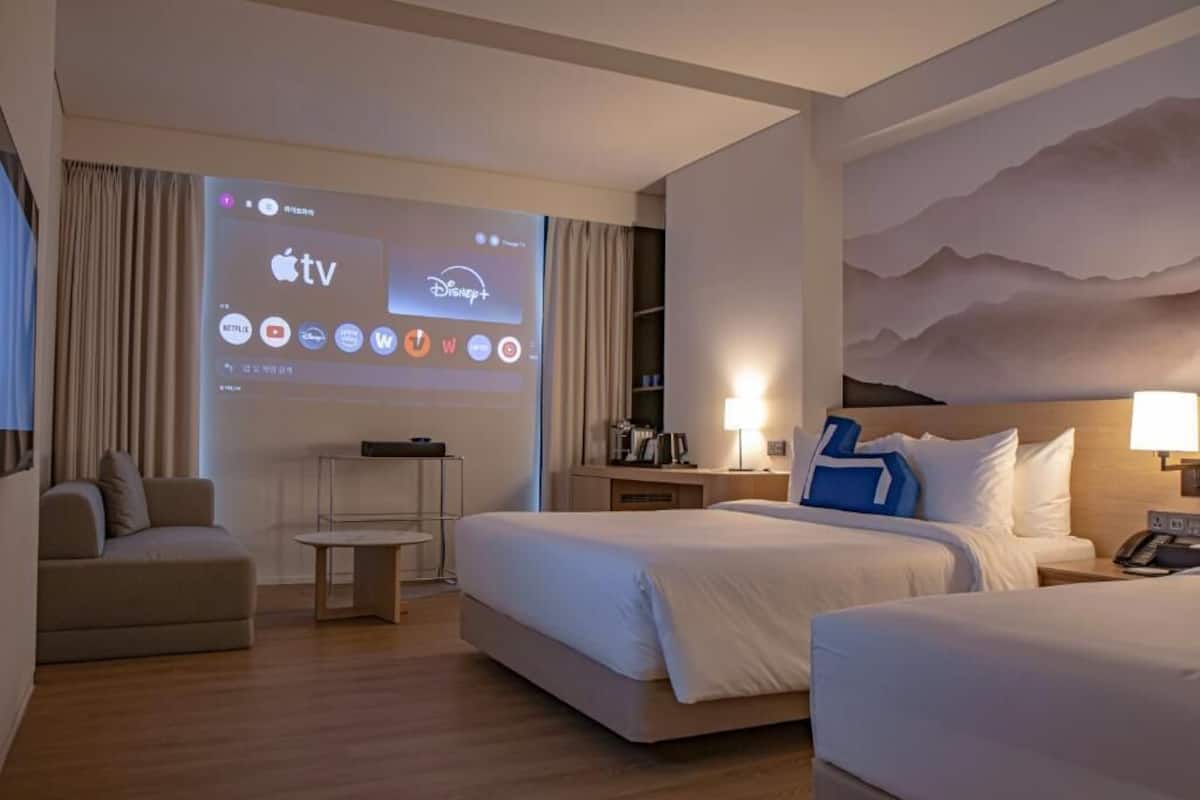 Ett hotellrum med en säng, ett skrivbord, en stol, en tv-skärm som visar strömnings­tjänster och en vägg med ett bergsmotiv.