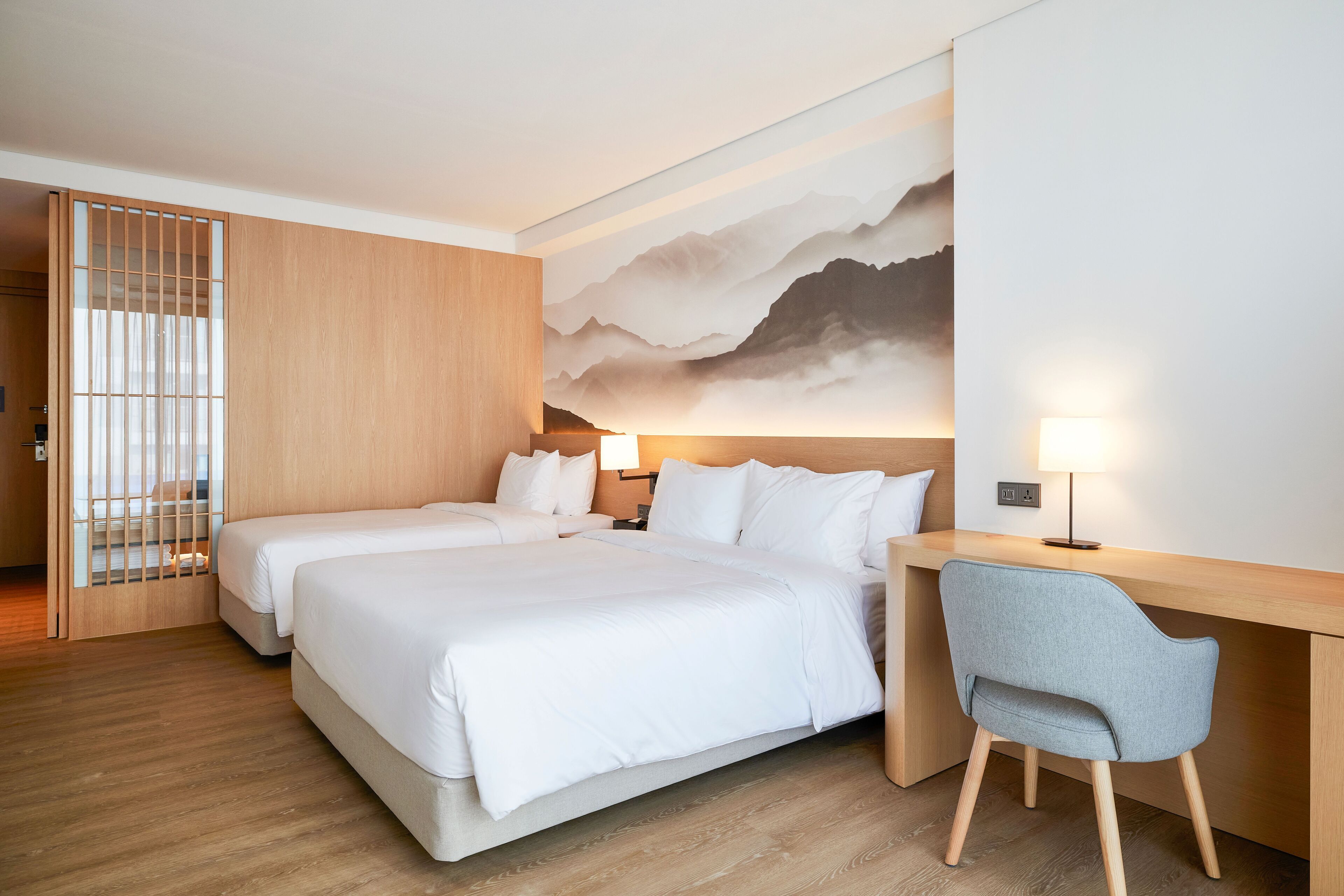 A hotel room with two beds, a desk, a chair, and a large wall mural.