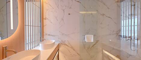 Un baño moderno con un lavamanos ovalado grande, ducha con cerramiento de vidrio y paredes de mármol.