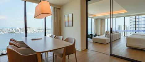 A modern hotel room with a dining area, a large window with a city view, and a separate living area with a sofa and a bed.