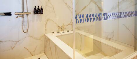 A modern bathroom with a glass-enclosed jacuzzi, marble walls, and a shower area.