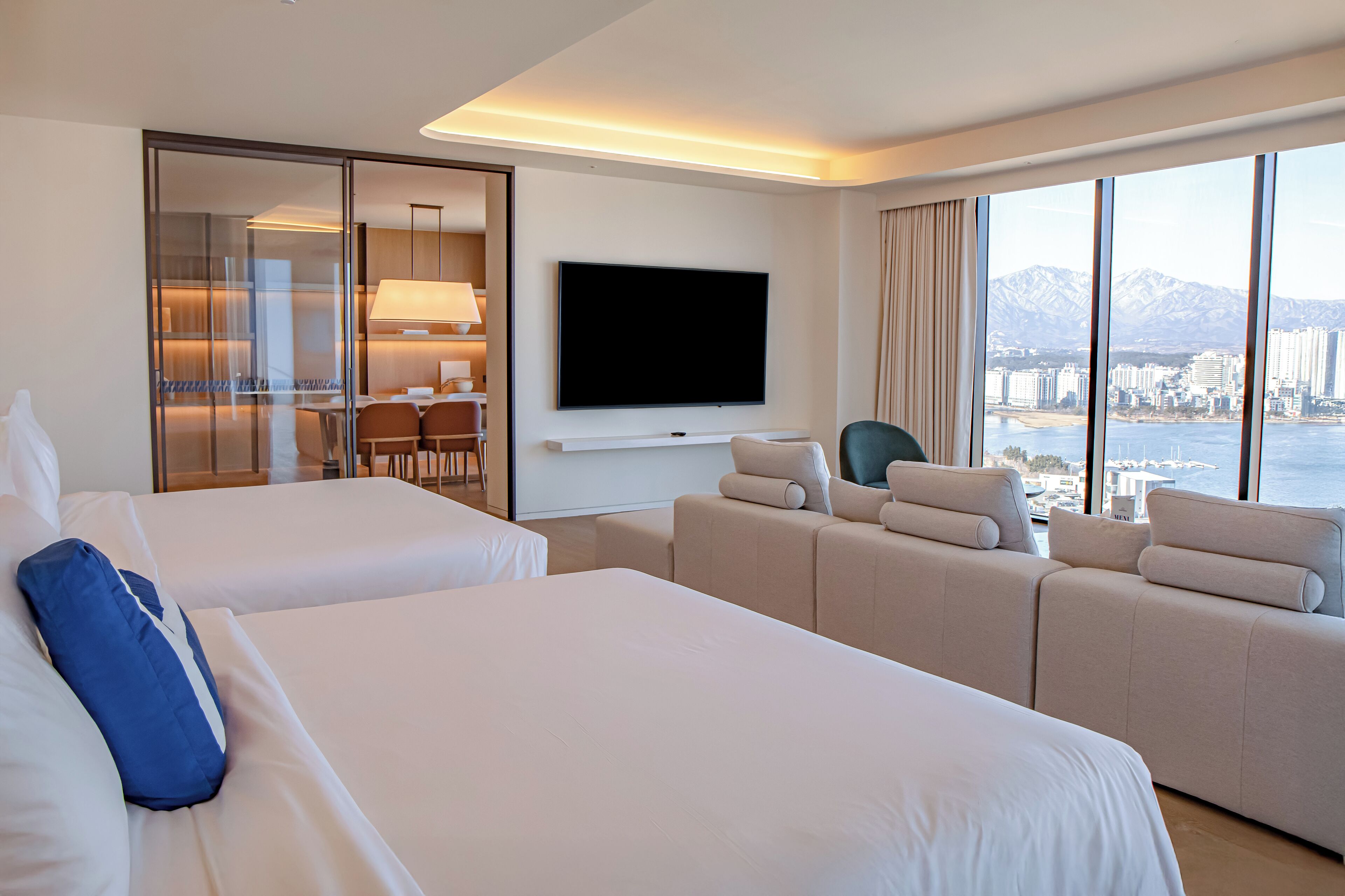 A hotel room with two beds, a sofa, a TV, and a city view.