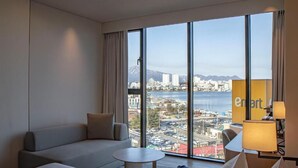 Una habitación de hotel con un ventanal grande, un sofá, una mesita y una lámpara.
